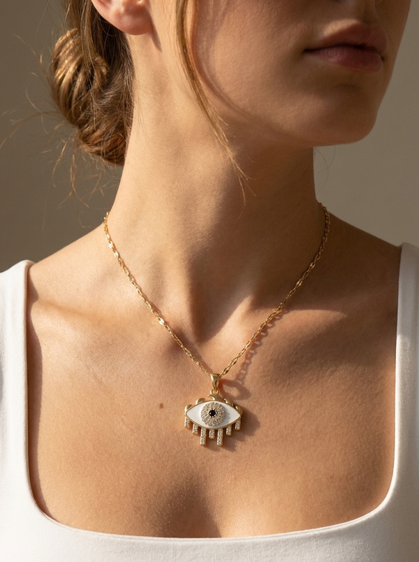 Naomi Kolye'nin detayı, zarif beyaz mina ve taşlarla süslü göz formu, paslanmaz çelikten yapılmış özel zincir ile birlikte lüks bir görünüm sunmaktadır. Klasik nazar boncuğu görünümüne modern bir yorum.